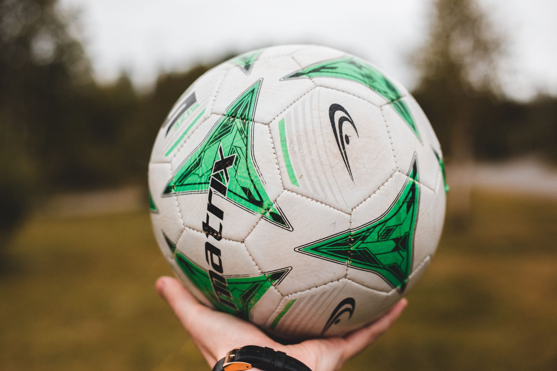 A photo of a hand holding a white fooball with green patterns on